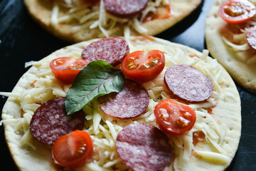 Mini Pizza With Cherry Tomatoes And Salami Sausages On A Wooden Background Natural Rustic, A Pizza Cutter And Ingridienty.