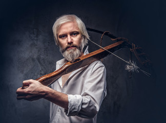 Studio portrait of a smiling handsome old man with a gray beard and white shirt holding a crossbow on shoulder.