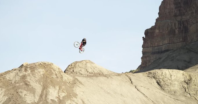 Slow motion pan left, mountain biker goes off jump in Utah