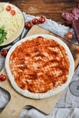 Ingredients for Pizza: basis dough, salami sausage, cherry tomatoes, grated cheese, tomato paste, herbs and arugula. Natural Wooden Background With Linen Napkin and Knife For Pizza