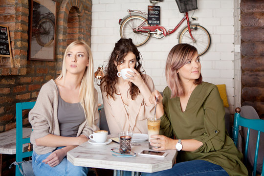  Three women at cafe drinking coffee, relaxing and enjoying their time. Lifestyle and friendship concepts