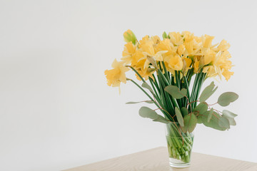 Yellow daffodils and eucalyptus in glass vase on wooden table