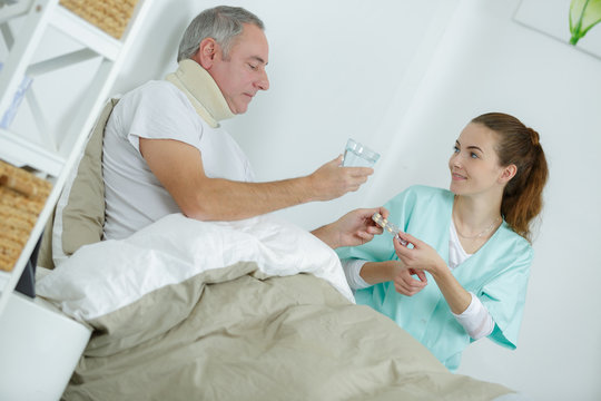 caregiver giving medication to middle-age man on bed