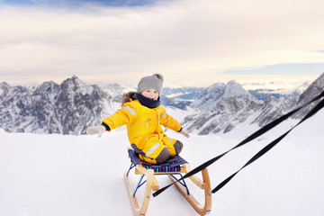Fototapeta na wymiar Cute caucasian little boy sledding in Alps mountains. Winter fun for family with kids