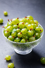 Gooseberries in glass bowl on black stone slate background.