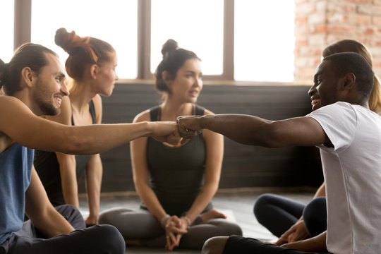 Smiling Sporty Fit African American And Caucasian Men Fist Bumping At Group Training Meeting In Gym Studio, Two Diverse Friends Greeting Or Supporting Team Motivation For Sport Yoga Teamwork Concept