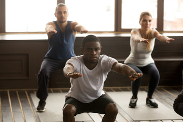 Young african american man doing squat exercise at group fitness training, sporty black guy focused...