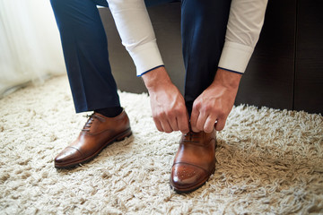 Businessman tying shoe laces indoors, close up. Man dressing up with elegant leather shoes. Groom...