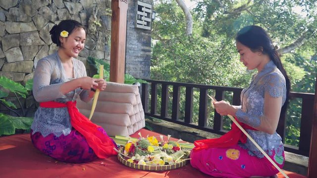 Two young balinese women chatting while making canang sari offerings in Ubud, Bali