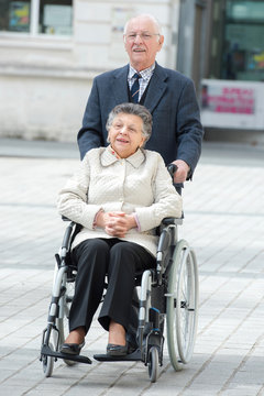 senior man pushing woman in wheelchair