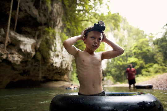 Young boy wearing a headlamp stands knee deep in water inside an inflatable ring.