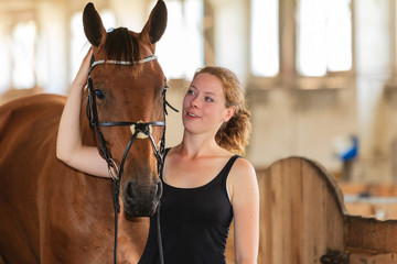 Jockey young girl petting and hugging brown horse