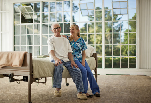 Smiling senior man being comforted by a female nurse inside his bedroom.