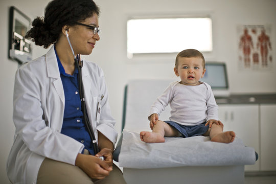 Female Doctor Looking At Baby Boy While Sitting In Hospital