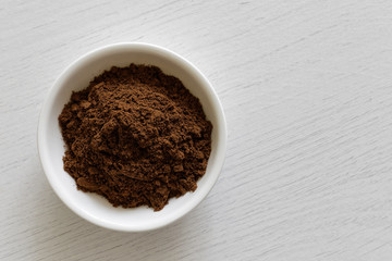 Ground allspice in white ceramic bowl isolated on white wood background from above.