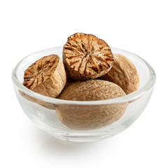 Dried whole and cut nutmegs in glass bowl isolated on white.