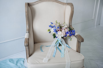 Wedding bouquet with blue wildflowers and peonies with blue and lace ribbons on a luxurious armchair
