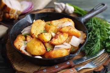 Hot roasted potatoes with bacon served with cutlery and greenery on cast iron frying pan, Ukrainian cuisine, countryside still life, homemade traditional meals concept