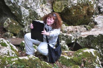 A young woman with a tablet computer sits among mossy limestone stones