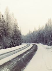 Wintry road, curve ahead. Snowy ground and forest. Image has a vintage effect applied.