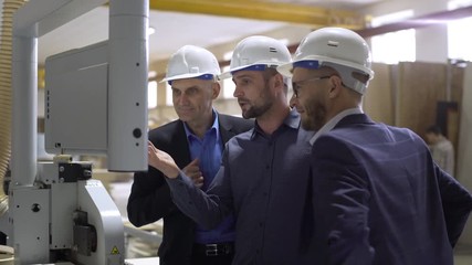 Portrait board of directors or sponsors in helmets watching and assessing new equipment in large facility, on furniture factory