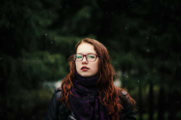 Beautiful young girl with red hair on a green natural background. Snow flakes are falling around. Red hair, painted with henna.