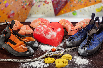 Two pairs of climbing shoes lie next to the climbing hook in the form of a heart. In the foreground, the rope passes through the carbine. In the background there is a climbing wall.