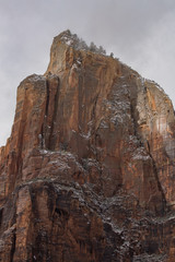 A single peak in the Court of the Patriarchs in Zion National park rises into the clouds with a dusting of snow on the ledges.