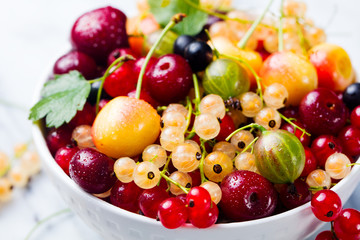 Assortment of fresh berries in white bowl. Marble background.