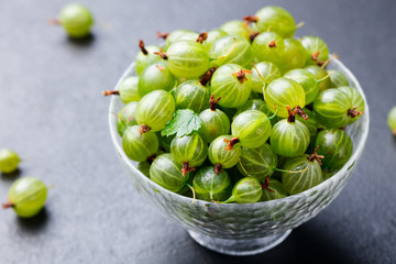 Gooseberries in glass bowl on black stone slate background.