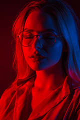 Pretty young woman in glasses posing with red and blue studio light