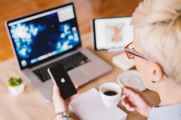 Rear view of businesswoman checking mobile while having a coffee break in the office.