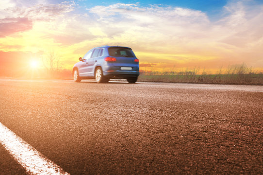 A Blue Car On The Countryside Road Against Night Sky With Sunset