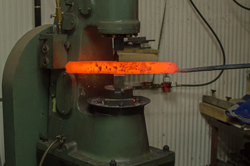 The blade smith is using a trip hammer to stretch out a red hot bar of Damascus steel.