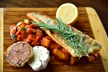 Pieczona ryba podana z warzywami w sosie pomidorywym.
