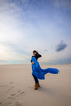 Romantic girl, wearing in a flying blue scarf, is walking in the desert