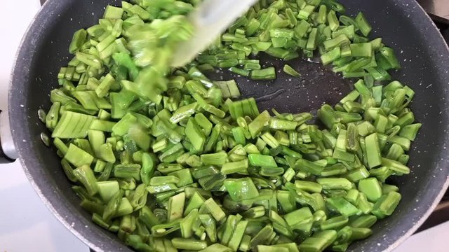 Time lapse of cooking slices of green Italian taccola, a kind of pea (Pisum sativum) in olive oil in a pot.
