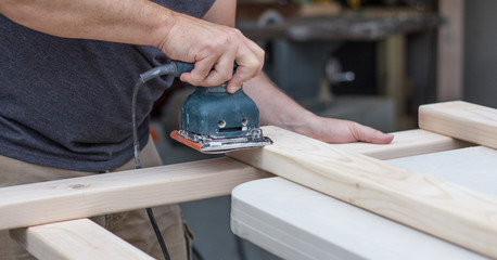 Close up of a man sanding down a wooden project on his workbench