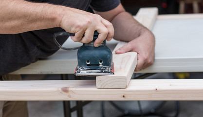 Close up of a man sanding down a wooden project on his workbench