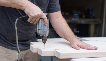 A close up of a man drilling into a wood project with an electric drill.
