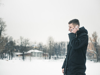 young man standing outside with mobile phone in his hands on a coldy freezing snowy day
