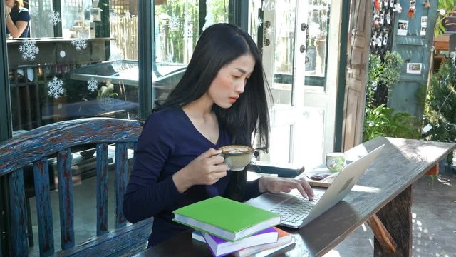 4k of young woman using laptop at cafe while drinking coffee