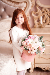 Smiling baby girl 4-5 year old holding flowers wearing white jacket in room. Looking at camera. Spring season.