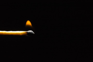 Burning match stick in the left corner of the frame on a black background
