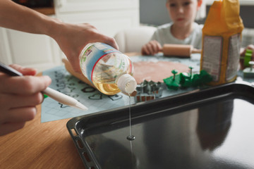 Mom and her son cook cookies in the cozy home kitchen. A trickle of vegetable oil in close-up. On the table there are cookie cutters green and silvery colors and a bag of flour.
