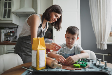 Mom and her son cook cookies in the cozy home kitchen. Mom helps the boy and gives him tins of cookies.