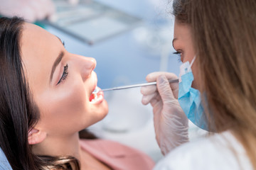 people, medicine, stomatology and health care concept - happy female dentist with mirror checking patient girl teeth up at dental clinic office while male assistant is waiting behind.