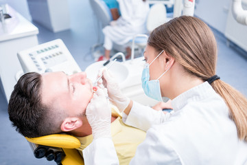 Obraz premium people, medicine, stomatology and health care concept - happy female dentist with mirror checking patient man teeth up at dental clinic office.