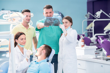 Naklejka na ściany i meble Dental medical team examining and working on young male patient.Dentist's office, while technician is reviewing xray.
