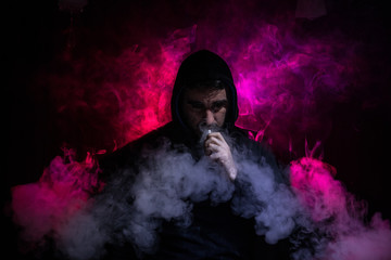 Vaping man holding a mod. A cloud of vapor. Black background. Vaping an electronic cigarette with a lot of smoke. Vape concept